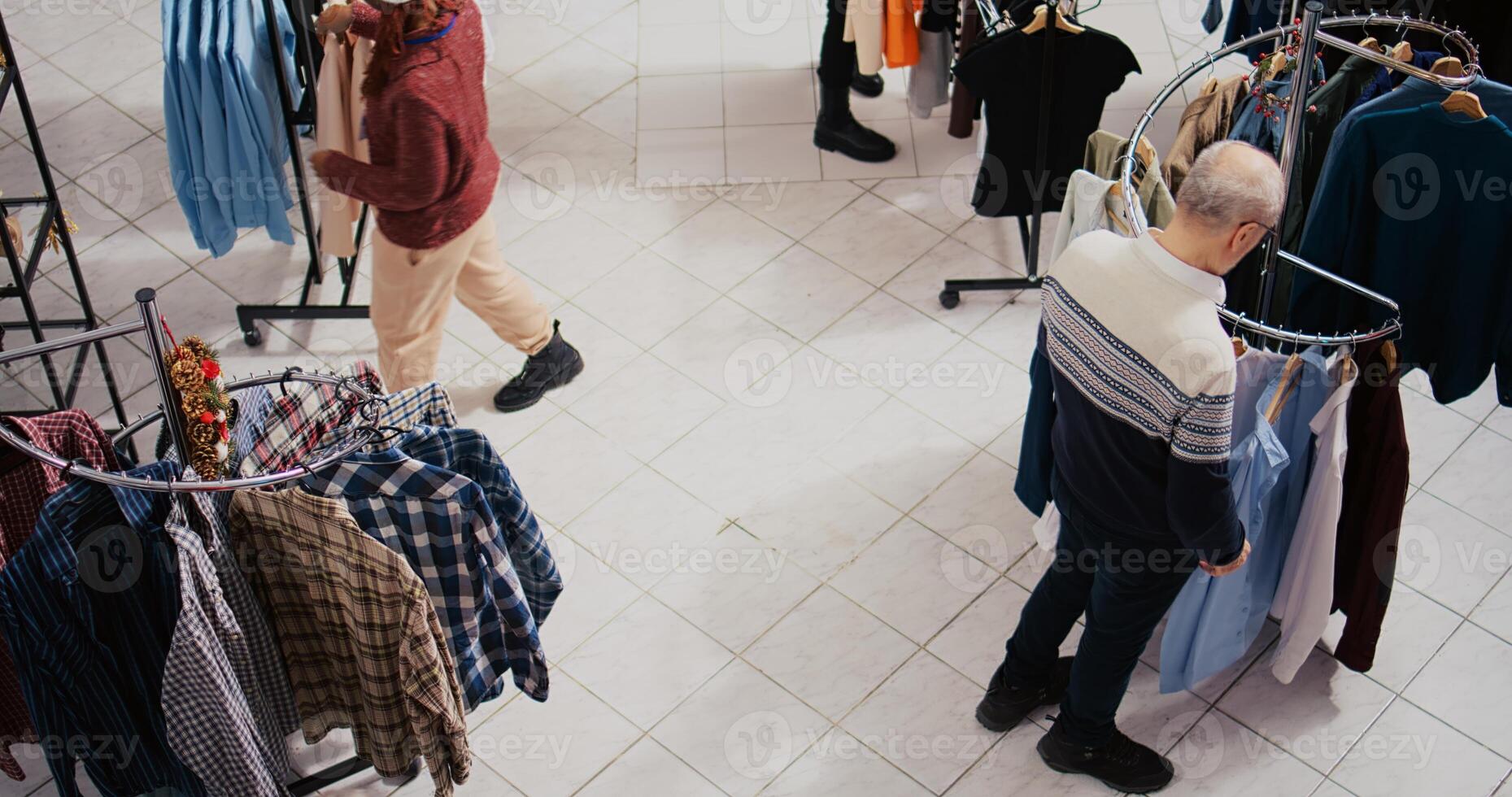 Top down view of clients walking around bustling shopping mall fashion shop aisles, looking to purchase clothes as presents for family and friends during Christmas promotional sales event photo
