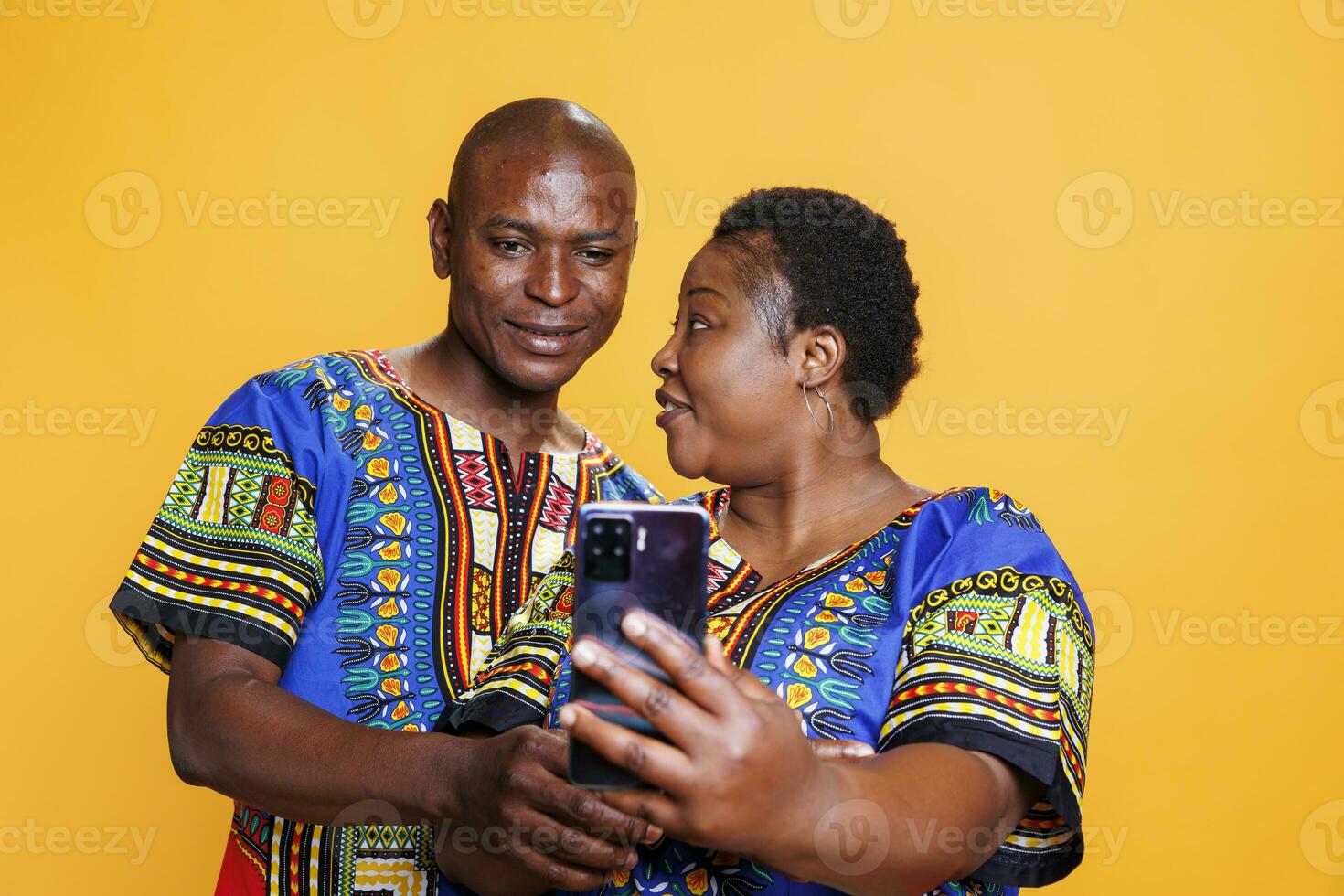 African american wife and husband couple holding mobile phone and taking selfie. Smiling man and woman pair making photo on mobile phone front camera together on studio background