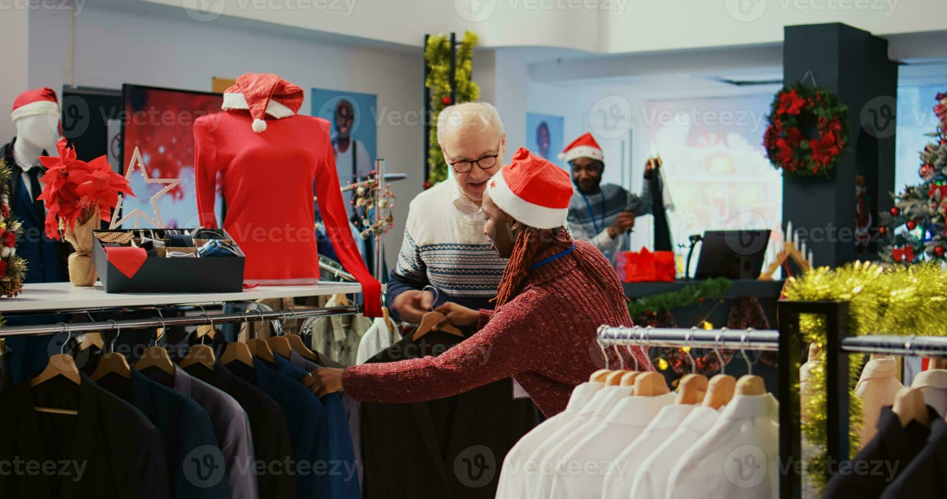Elderly client being helped by retail assistant in festive decorated clothing store to determine if stylish blazer is the right fit. Employee assisting aged man in Christmas ornate fashion shop photo