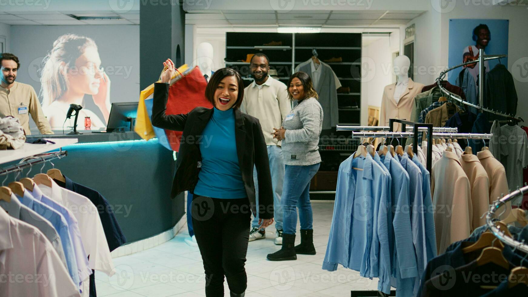 Asian customer doing dance moves with shopping bags, feeling happy after making purchase at cash register. Young woman dancing and buying trendy clothes at shopping mall. Tripod shot. photo