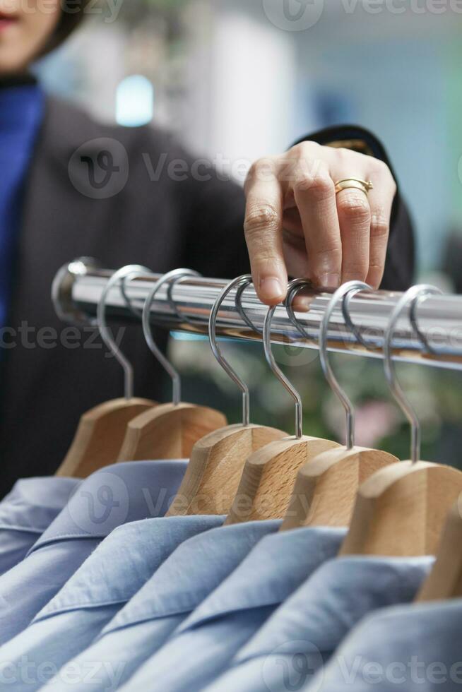 Shopping mall boutique seller hand adjusting and exploring apparel on rack closeup. Seller arm managing merchandise inventory and counting clothes in stock while working in outlet photo