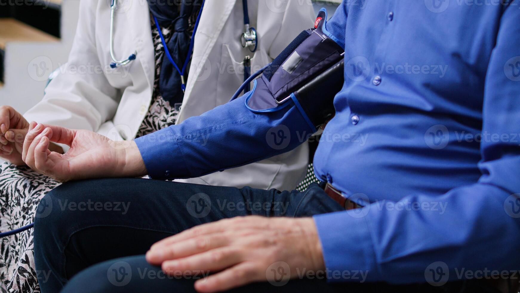 Elderly medic using medical tonometer to measure patient pulse pressure and hypertension, doing cardiology examination in hospital waiting room. Senior man attending checkup visit. Medicine concept photo