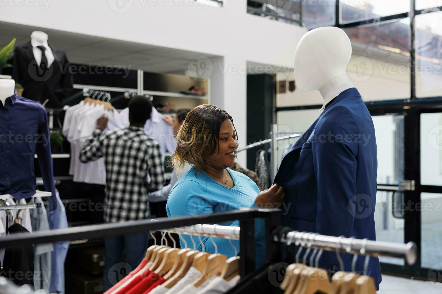 African american customer looking at formal blue suit, analyzing material in clothing store. Shopaholic woman checking new fashion collection, shopping for fashionable clothes in boutique photo