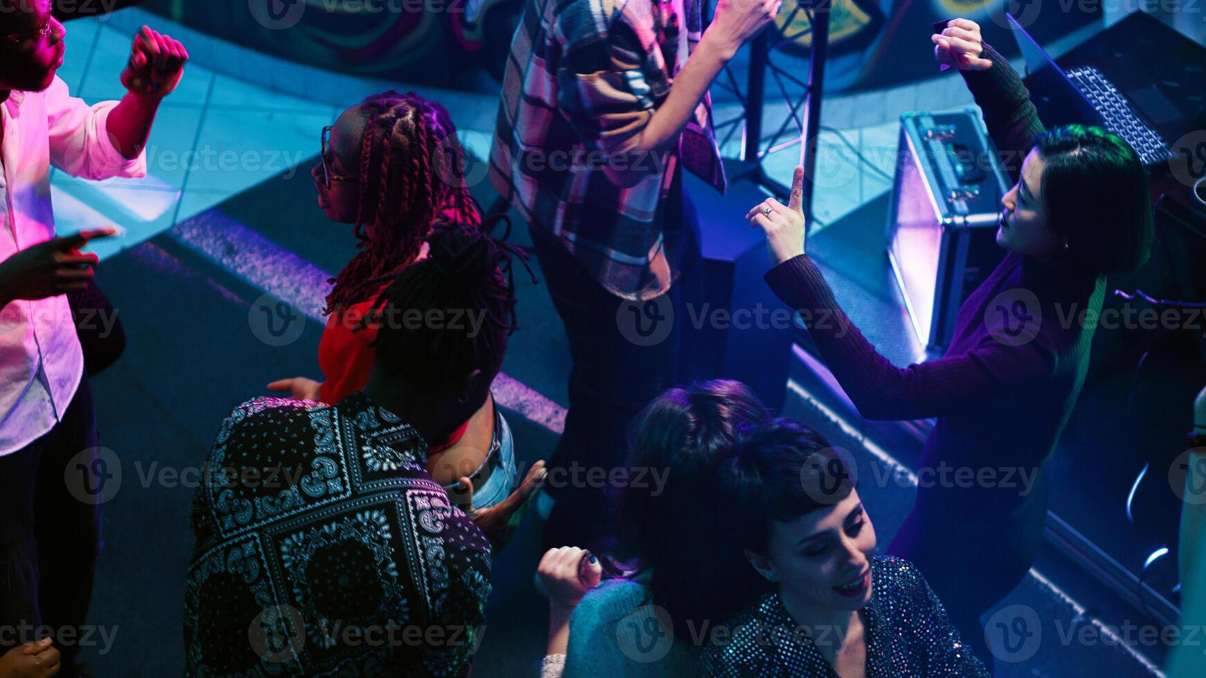 Young people doing funky dance moves on dance floor, enjoying nightlife with electronic music at club. Happy group of friends dancing and partying, having fun at nightclub. Handheld shot. photo