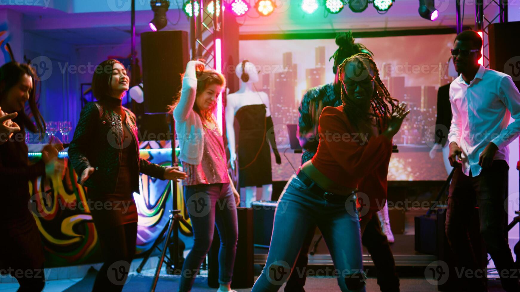 Funky people partying on dance floor enjoying electronic music party at nightclub. Group of happy friends dancing and partying together, having fun at social gathering. Handheld shot. photo