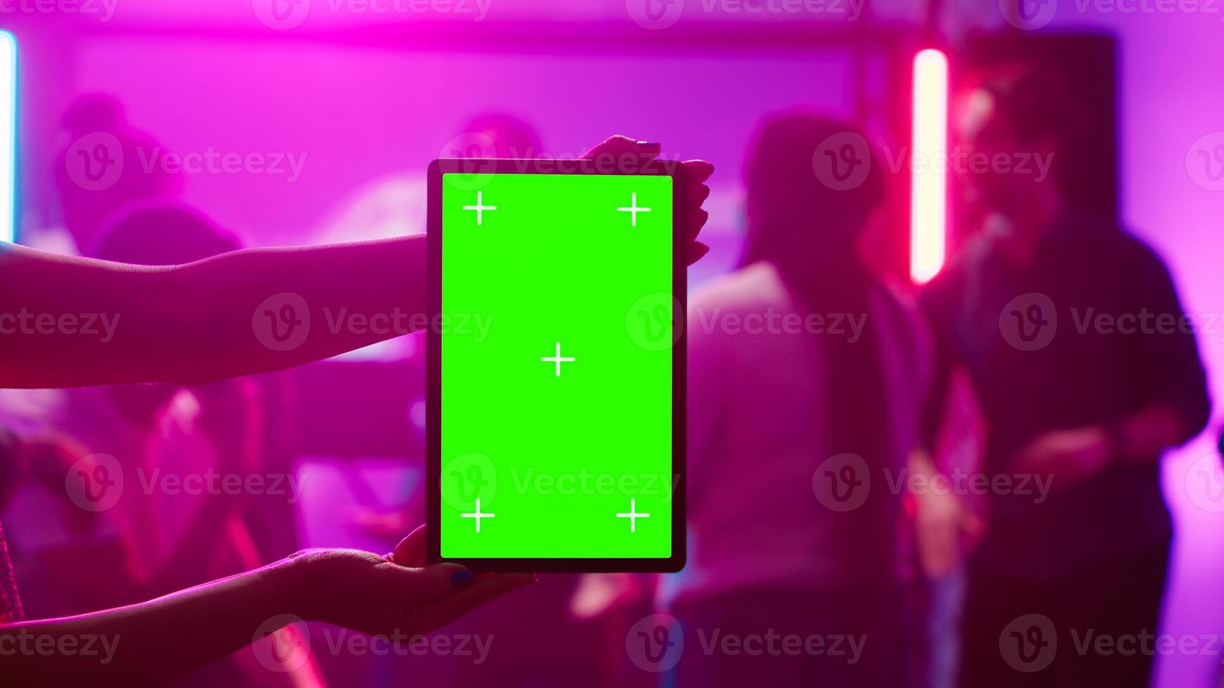 Woman holding greenscreen tablet at club and showing isolated display during dance party. Young funky adult using chroma key mockup template with blank copyspace on device screen. photo