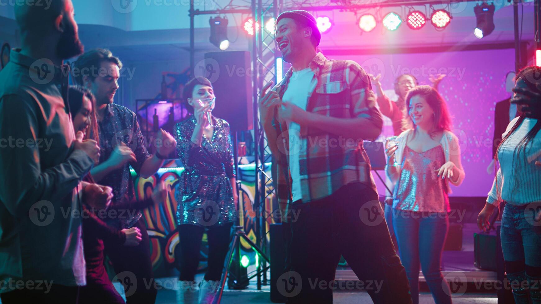 Young persons at underground club and having fun with electronic music mix, partying on performance show. Group of people feeling joyful enjoying celebration, social gathering. Handheld shot. photo
