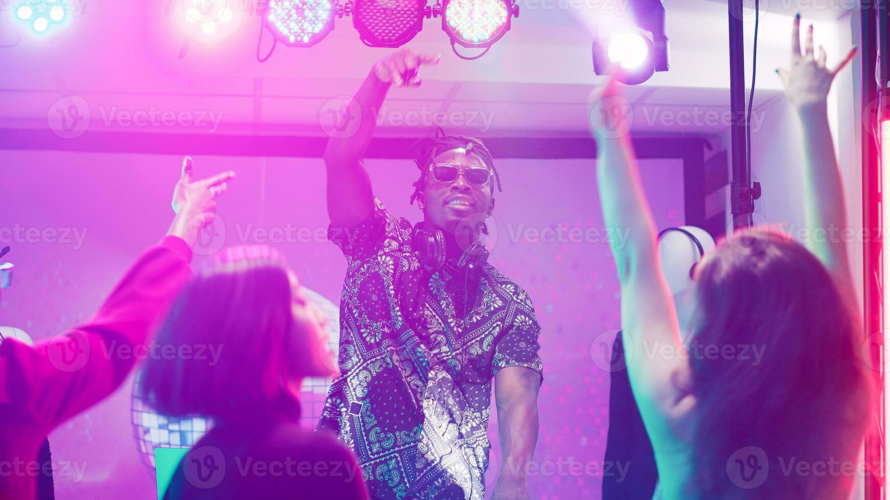 africano americano DJ mezcla audio en etapa a Club nocturno, frio hombre ir de fiesta con grupo de personas en danza piso. miedoso adulto creando electrónico mezcla sonidos a panel estación, discotecas. trípode disparo. foto