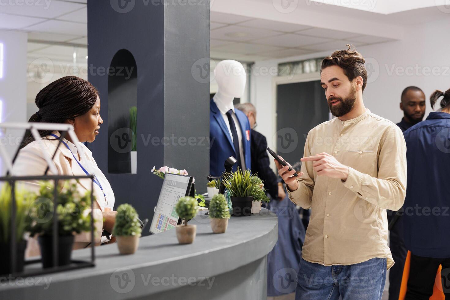 joven hombre cliente utilizando móvil lealtad programa aplicación mientras en pie a revisa cajero mostrador en ropa almacenar. comprador comprando ropa en compras centro comercial pago con teléfono inteligente foto