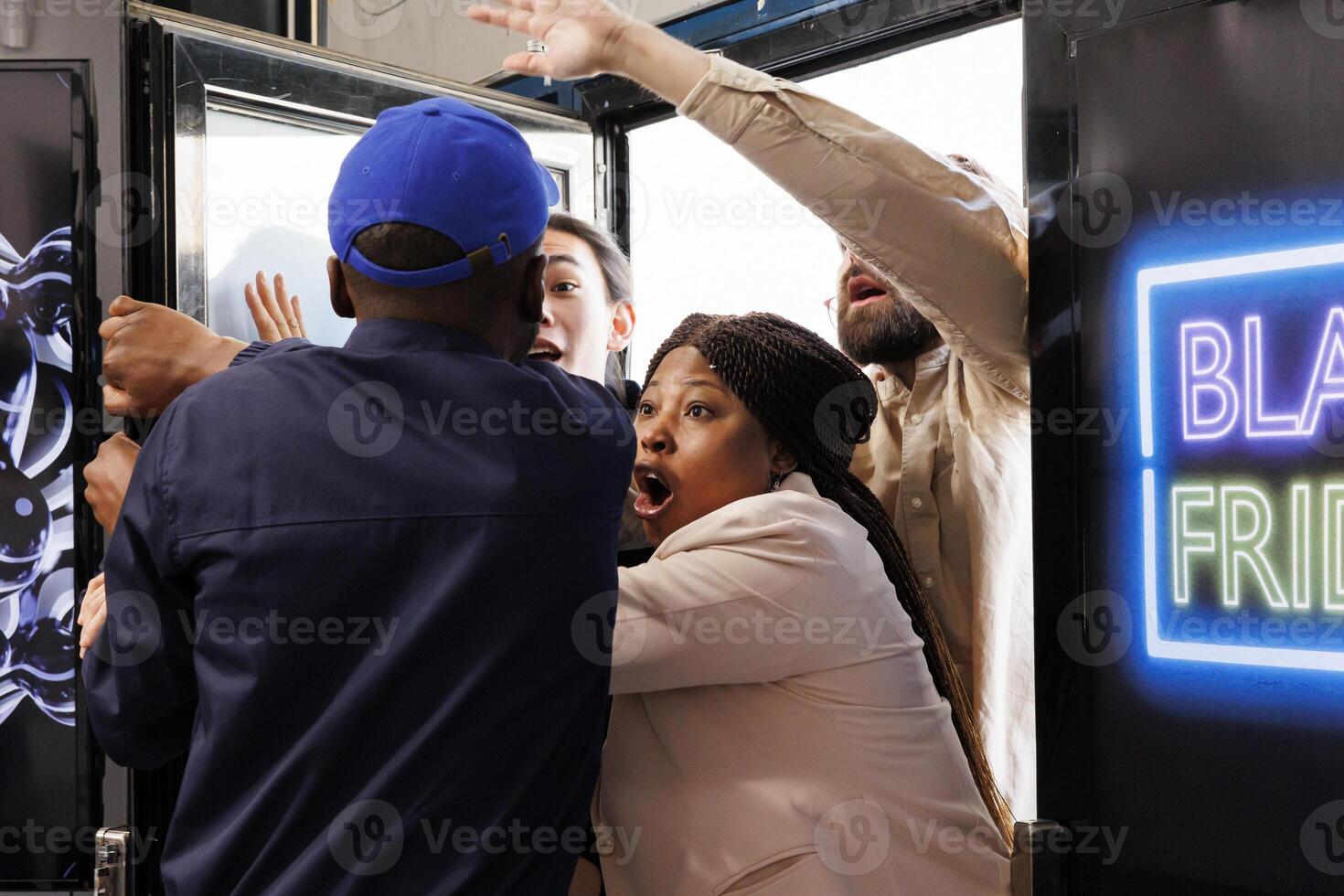 Frenzy diverse people shoppers breaking into store, pushing security guard and running into shopping mall to get best deals during Black Friday sales. Police officer trying to control aggressive crowd photo