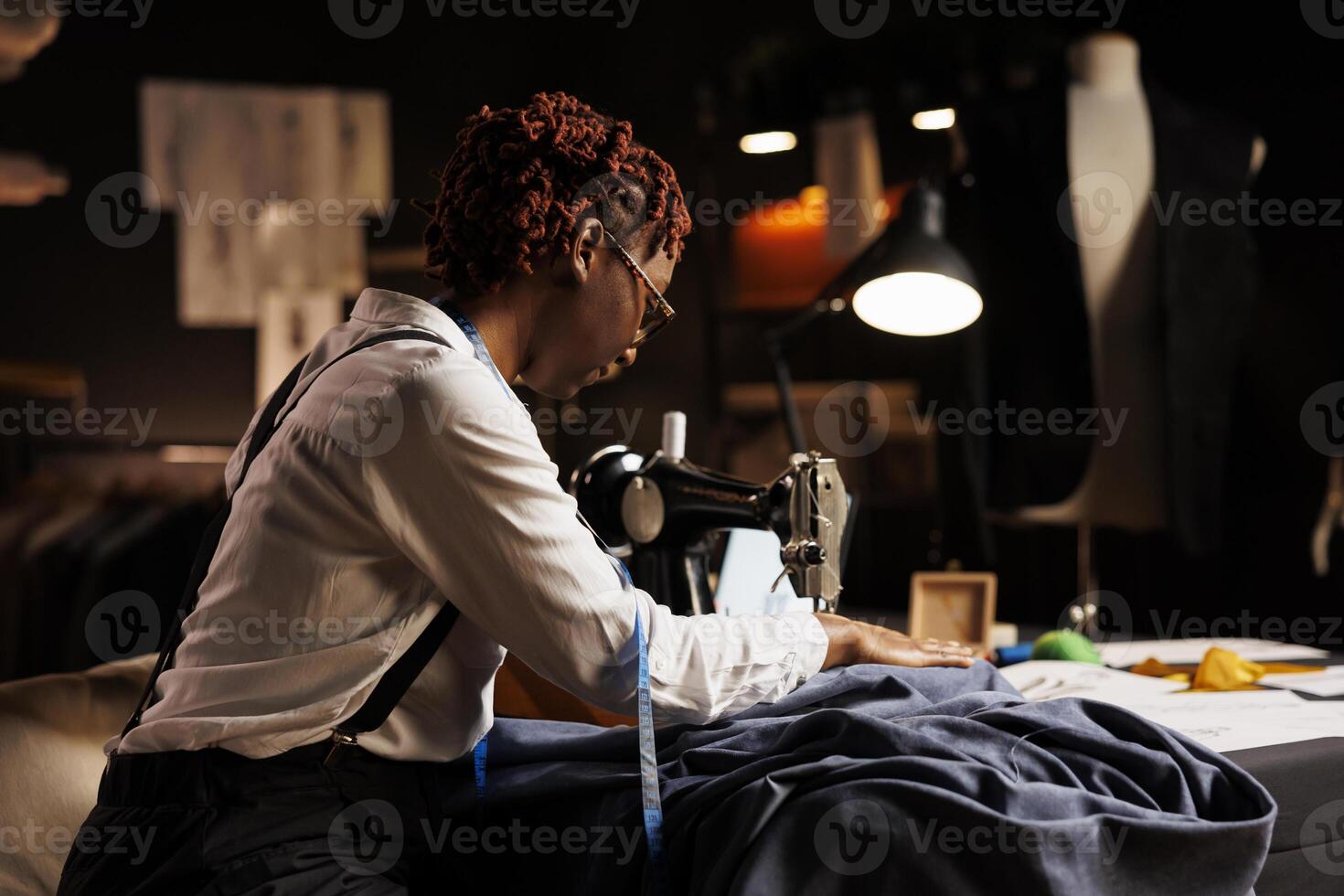 Experienced seamstress sewing textile garment for upcoming client bespoke sartorial comission. Skilled couturier using professional tailoring machine in atelier shop workspace photo
