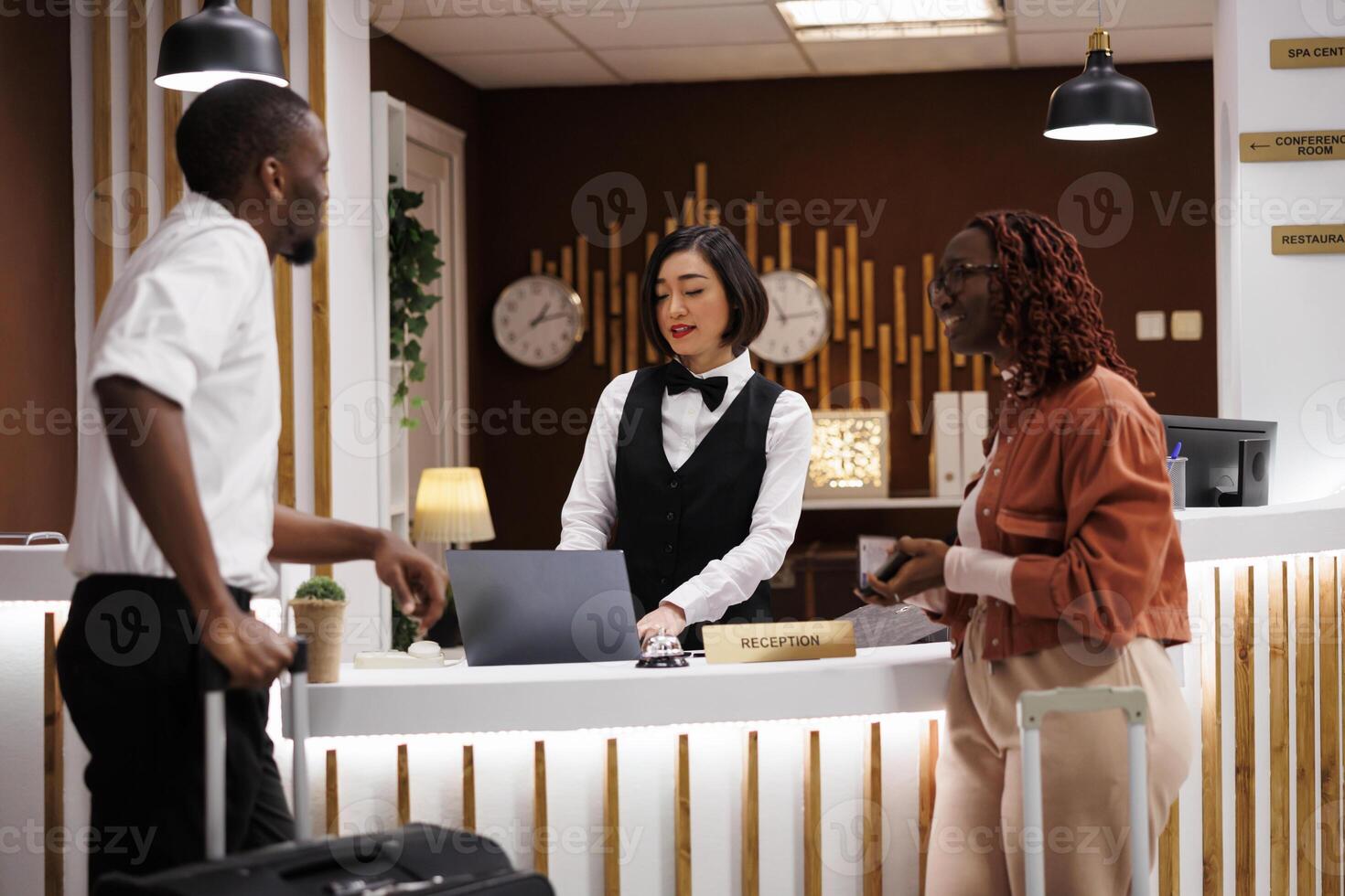 Employee talking to guests in hallway, asking about booking information to find accommodation record. Reception staff doing check in process at counter desk in lobby, hotel registration. photo