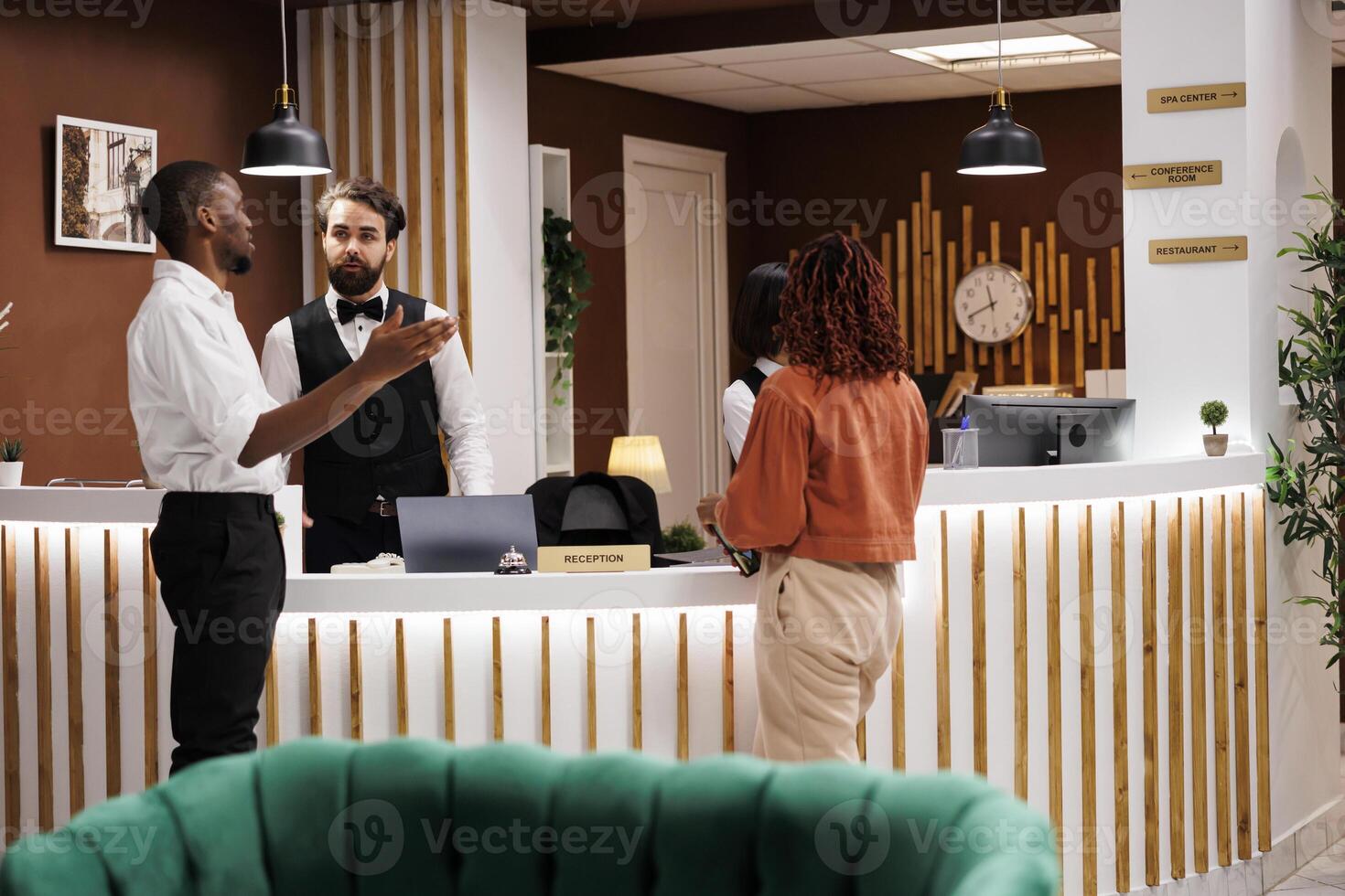 Hotel worker giving excellent service to guests at reception counter, talking about room accommodation after doing registration check in. Young man welcoming tourists at modern resort. photo