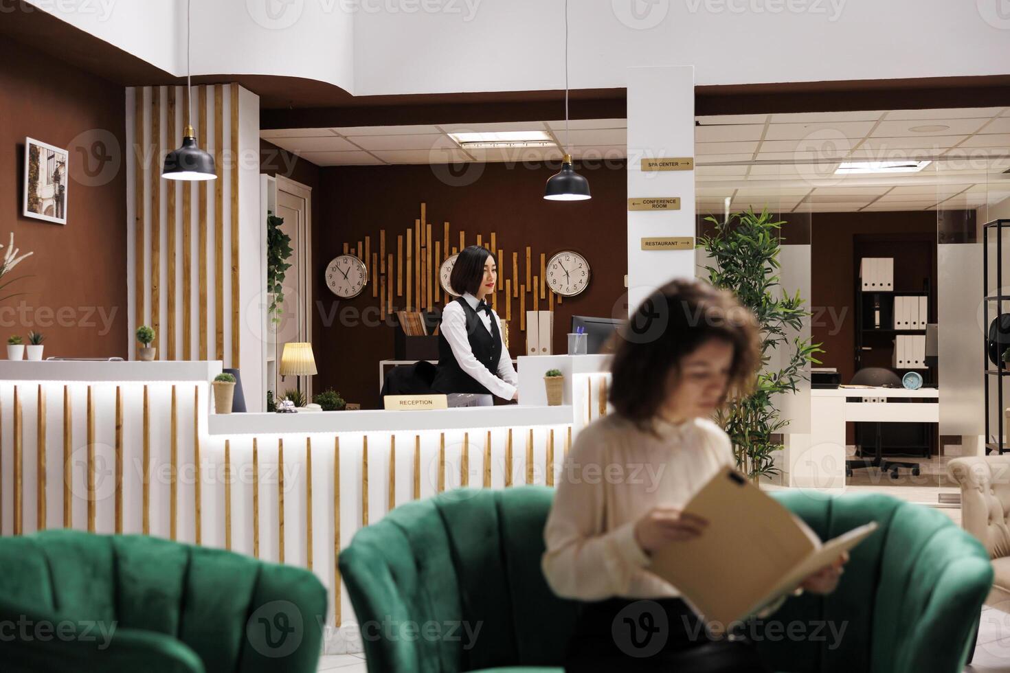 Woman working at hotel counter to check in guests and help with accommodation, luxury resort. Female receptionist at front desk checking registration forms before booking rooms. photo