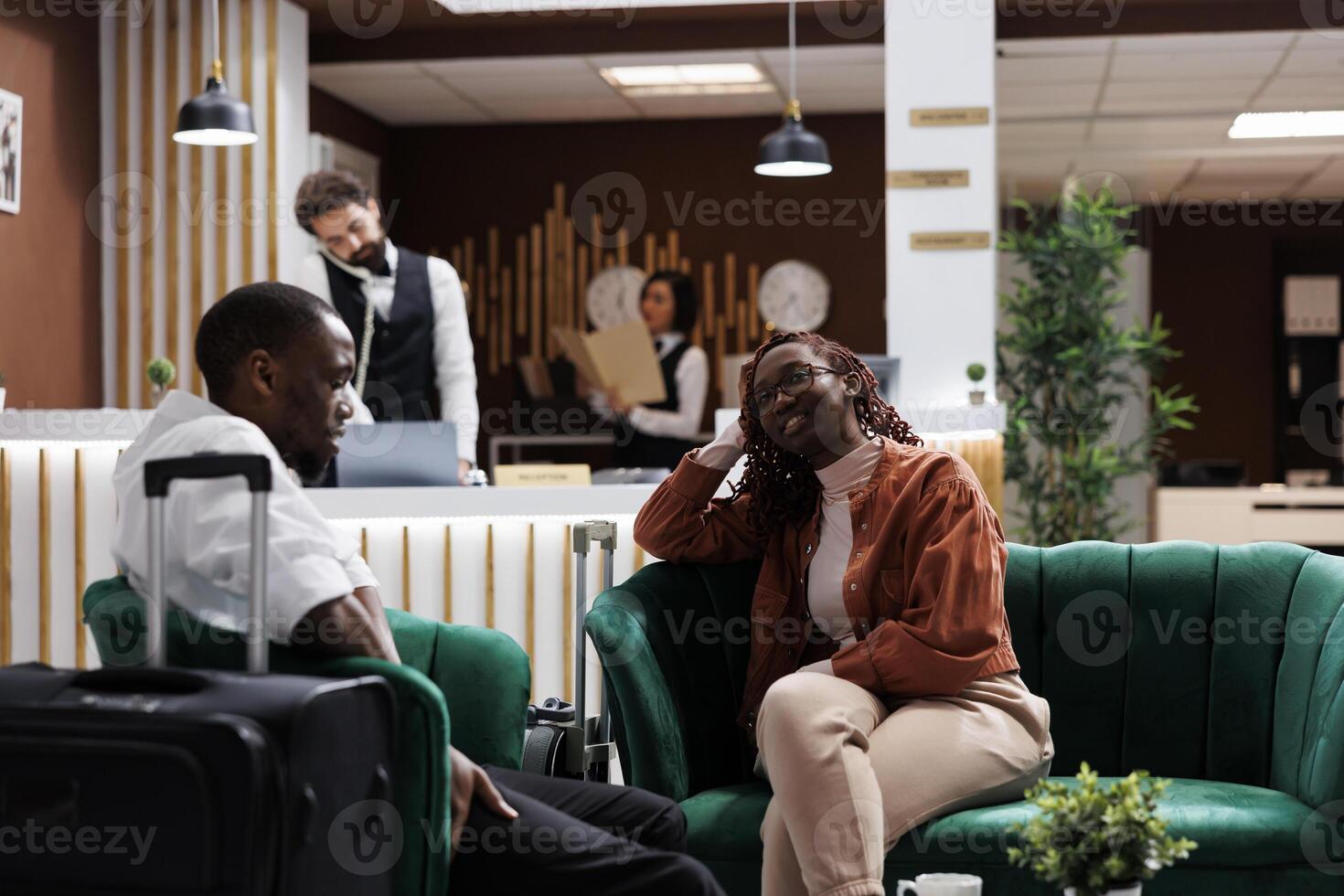 Happy people relaxing in lounge area before doing check in procedure to receive room card key, booking reservation. African american guests arriving at luxury hotel, waiting on couch. photo