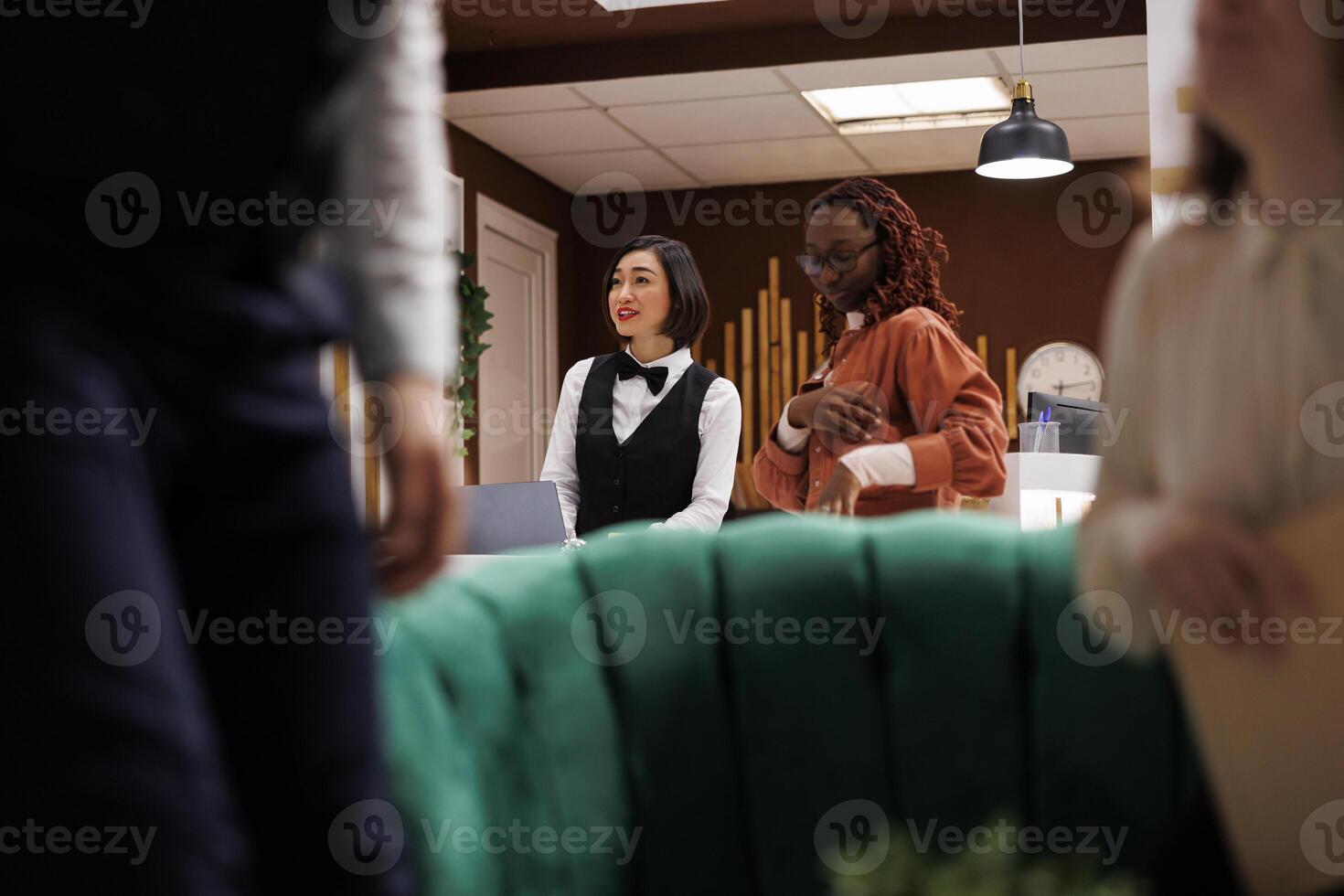 Hotel staff talking to couple in lobby, asking about room reservation booking before helping with check in procedure. Receptionist at front desk filling in registration forms, friendly service. photo