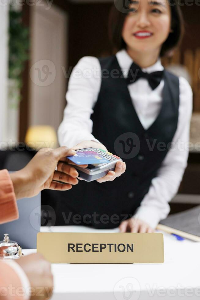 Woman guest paying at pos terminal in luxury resort, using electronic transaction at registration process. Female tourist holding credit card at reception front desk, welcome people. Close up. photo