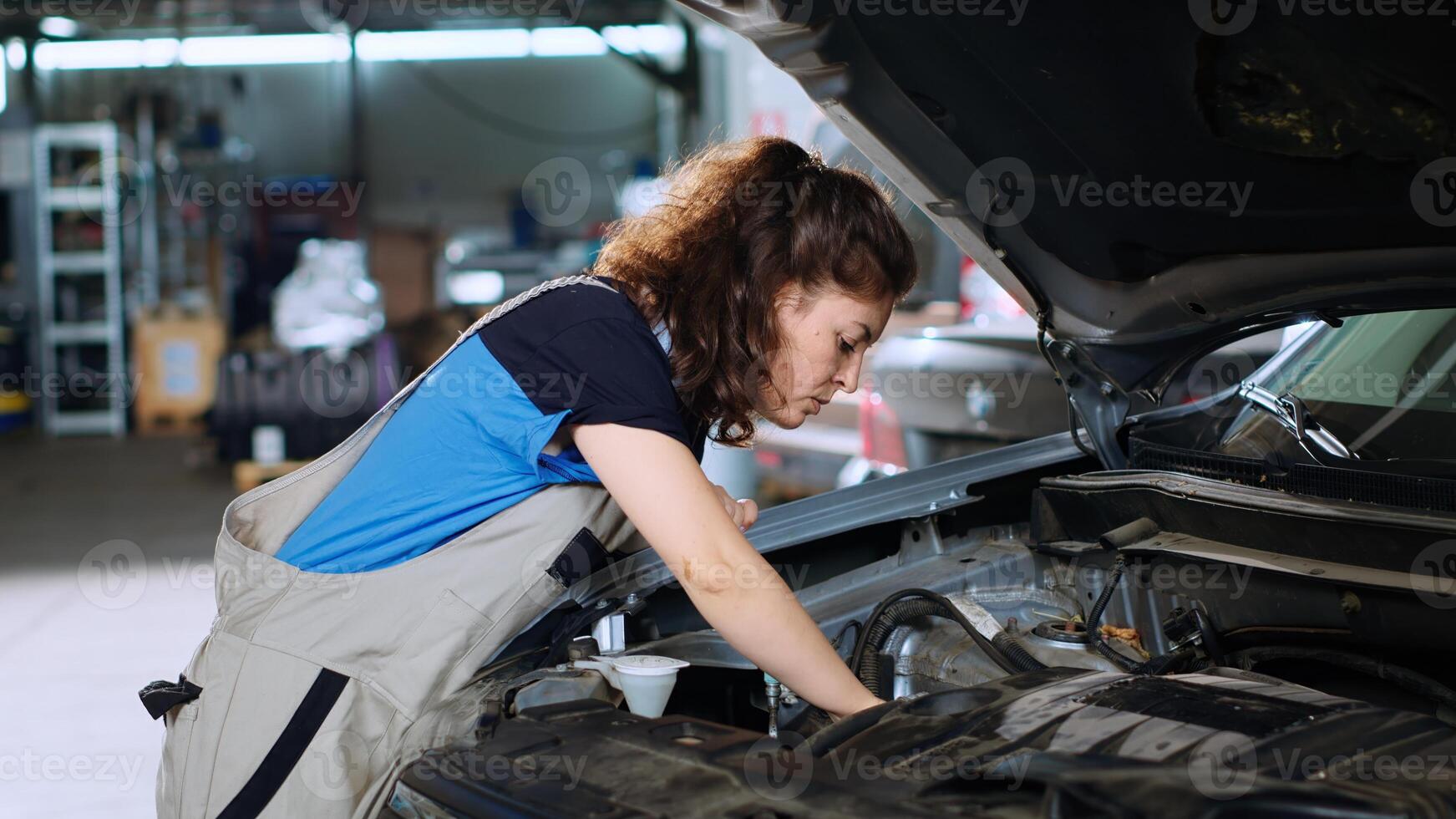 Hardworking mechanic in garage using torque wrench to tighten bolts inside opened up vehicle after changing lubricant. Car service employee doing maintenance on automobile, wiping leftover mess photo