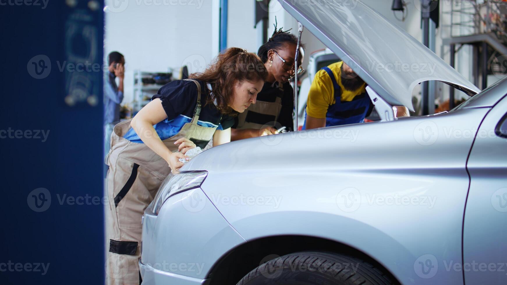 Team of mechanics in car service using inspection lamp to fix automobile in need of repairments. Colleagues service broken vehicle, checking for faulty engine using professional tools, dolly out shot photo