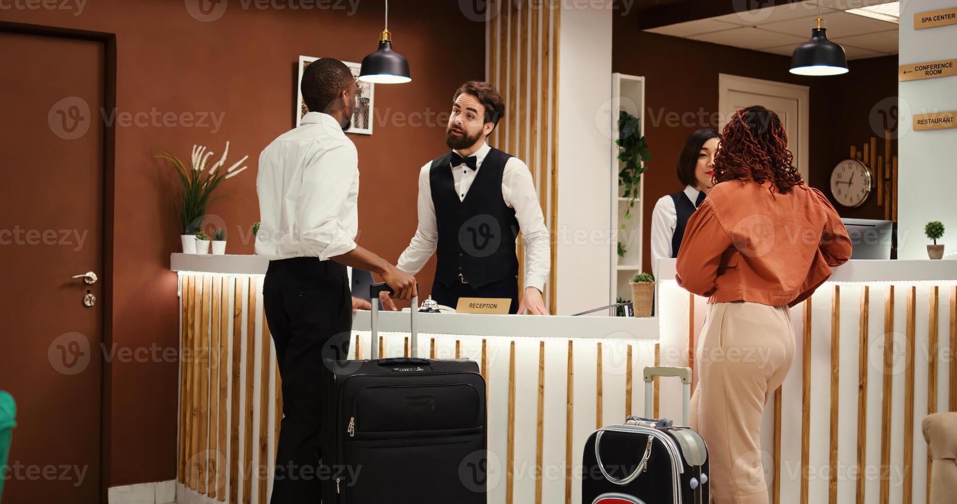 Professional friendly receptionist team greeting tourists on holiday trip in resort lobby. Helpful concierge personnel welcoming guests at hotel reception front desk during check in process photo
