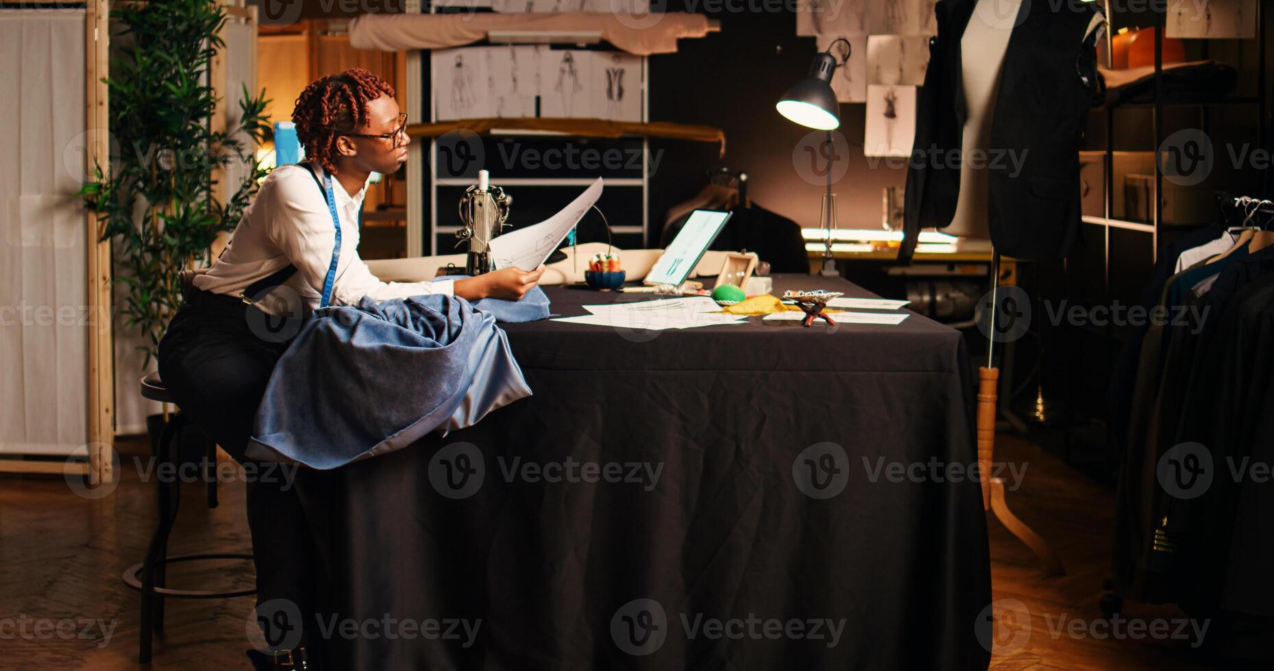 Seamstress using sewing machine to design and craft fashion items at workstation. Professional tailor working with handcraft equipment and tools, creating tailored custom made clothes. photo