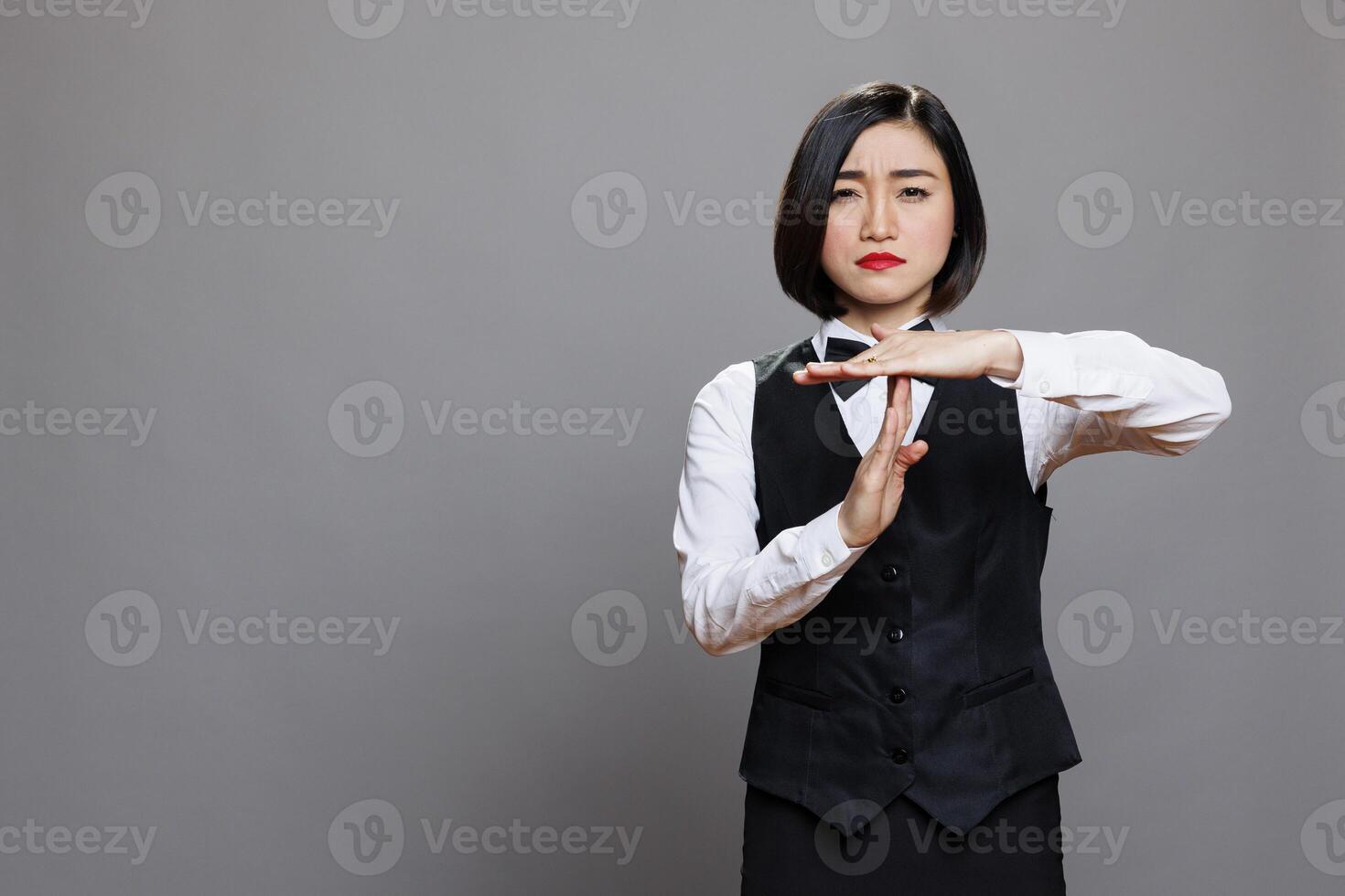 Confident asian waitress wearing uniform showing timeout sign with arms portrait. Restaurant serious woman employee asking to take break while making gesture with hands and looking at camera photo