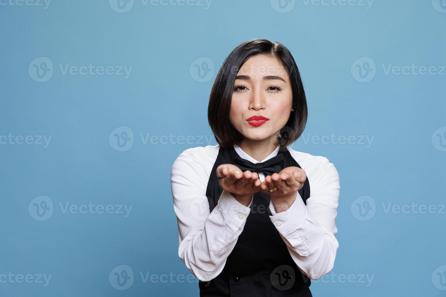 Smiling attractive asian waitress wearing uniform sending air kiss and looking at camera. Beautiful young woman receptionist expressing love and affection portrait in studio photo