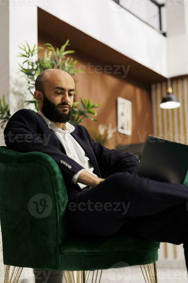 White collar worker in suit at hotel, travelling to be present at important business meeting with corporate CEO. Formal person working on laptop to do last minute changes on project. photo