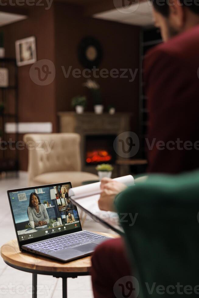 Entrepreneur attends videocall meeting on laptop, sitting in lounge area at modern hotel. Talking to coworkers on online teleconference, killing time before doing check in process. photo