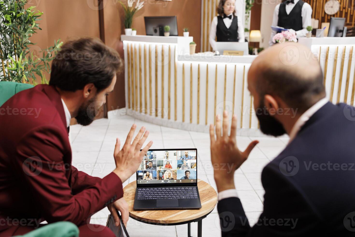 Management team attend videocall together in reception of luxury hotel, meeting with coworkers while they are travelling on business trip. Two managers in lounge area using videoconference call. photo