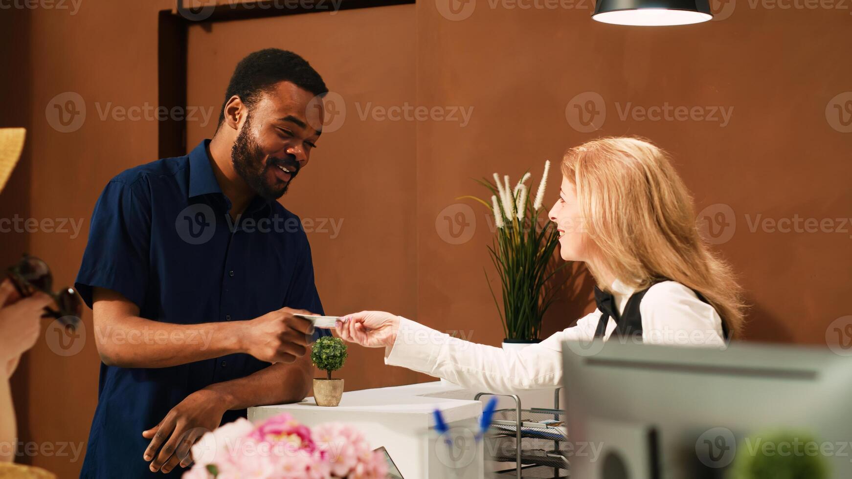 Guest taking room key card from front desk staff, receiving access to accommodation upon his arrival at tropical hotel. Male tourist finishing check in process at reception lobby. Handheld shot. photo
