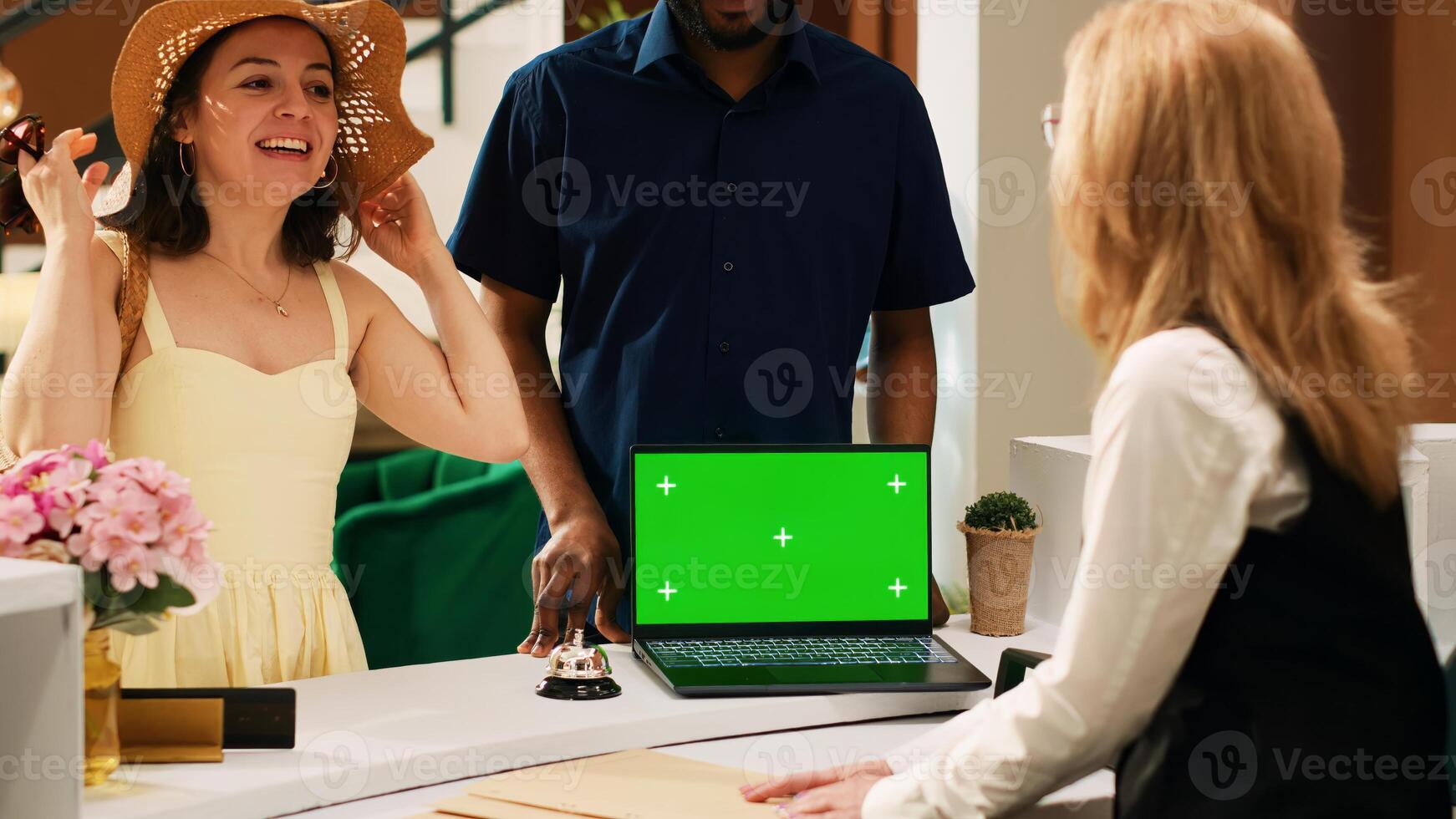Hotel worker welcoming guests at reception, using greenscreen template on laptop at front desk. Employee talking to people in lobby, working with isolated mockup display at resort. Tipod shot. photo