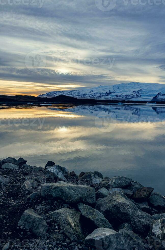 Scandinavian frosty lake near highlands forming nordic winter landscape at sunset, large body of water and snowy mountains in icelandic scenery. Frozen fields in spectacular countryside. photo