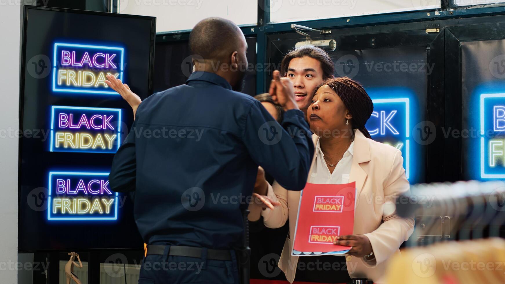 Angry clients pushing security guard, forcing to break red tape and buy clothes on promotional prices. Black friday anxious behaviour, crowd of diverse people in line at clothing store. Handheld shot. photo