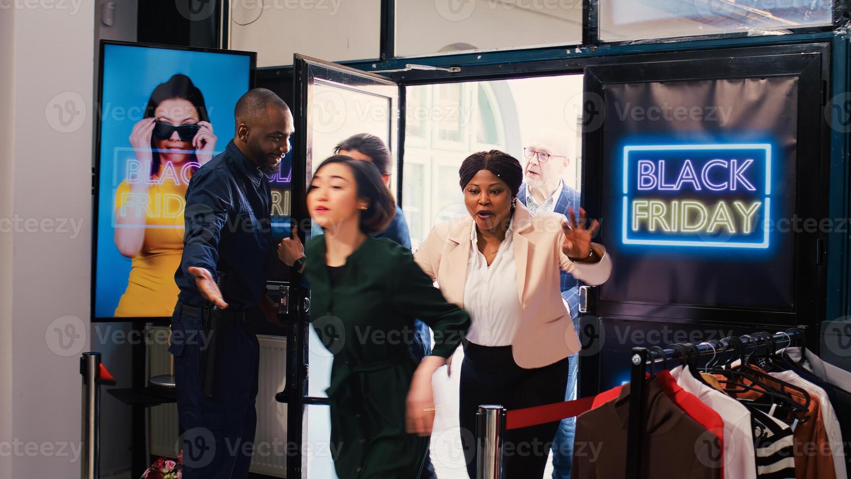 Shoppers push red tape entering store, looking to buy clothes during black friday big sales. Security guard working under pressure with crowd of anxious crazy customers waiting outside. photo