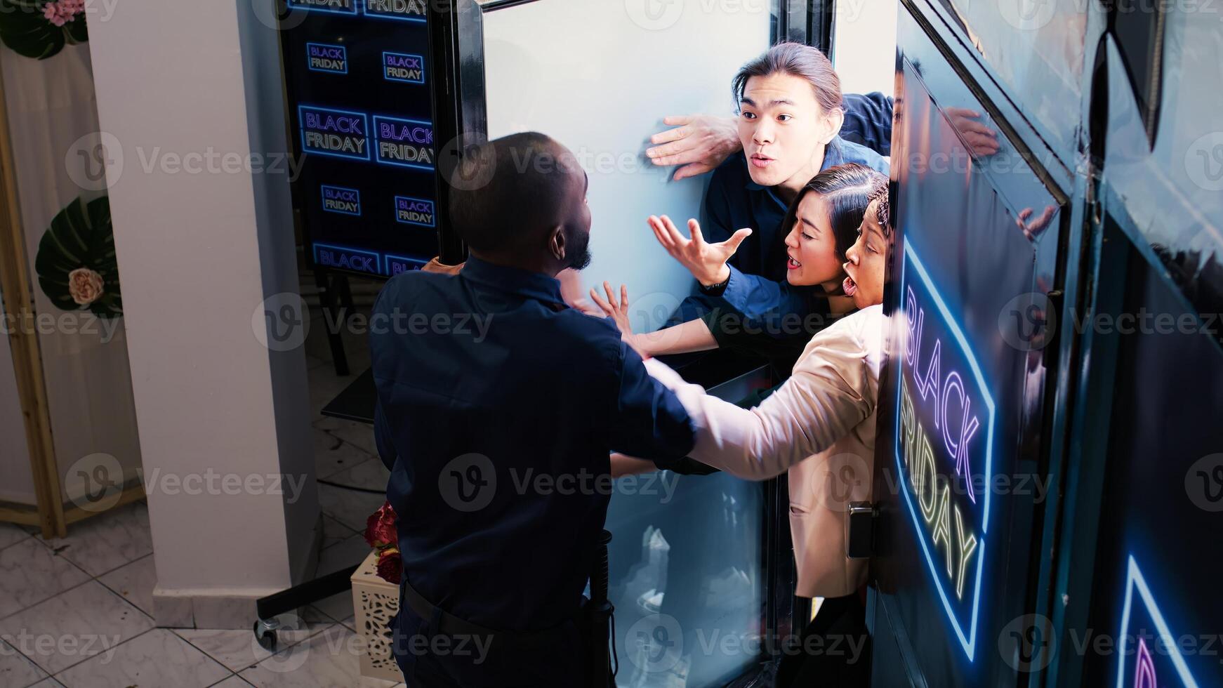 Impatient shoppers fighting staff to enter clothing store, pushing african american security guard on black friday. Agent holding back angry eager crowd, trying to keep door closed. Crowd control. photo