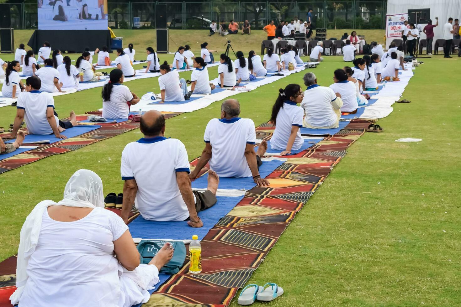 New Delhi, India, June 21, 2023 - Group Yoga exercise session for people at Yamuna Sports Complex in Delhi on International Yoga Day, Big group of adults attending yoga class in cricket stadium photo
