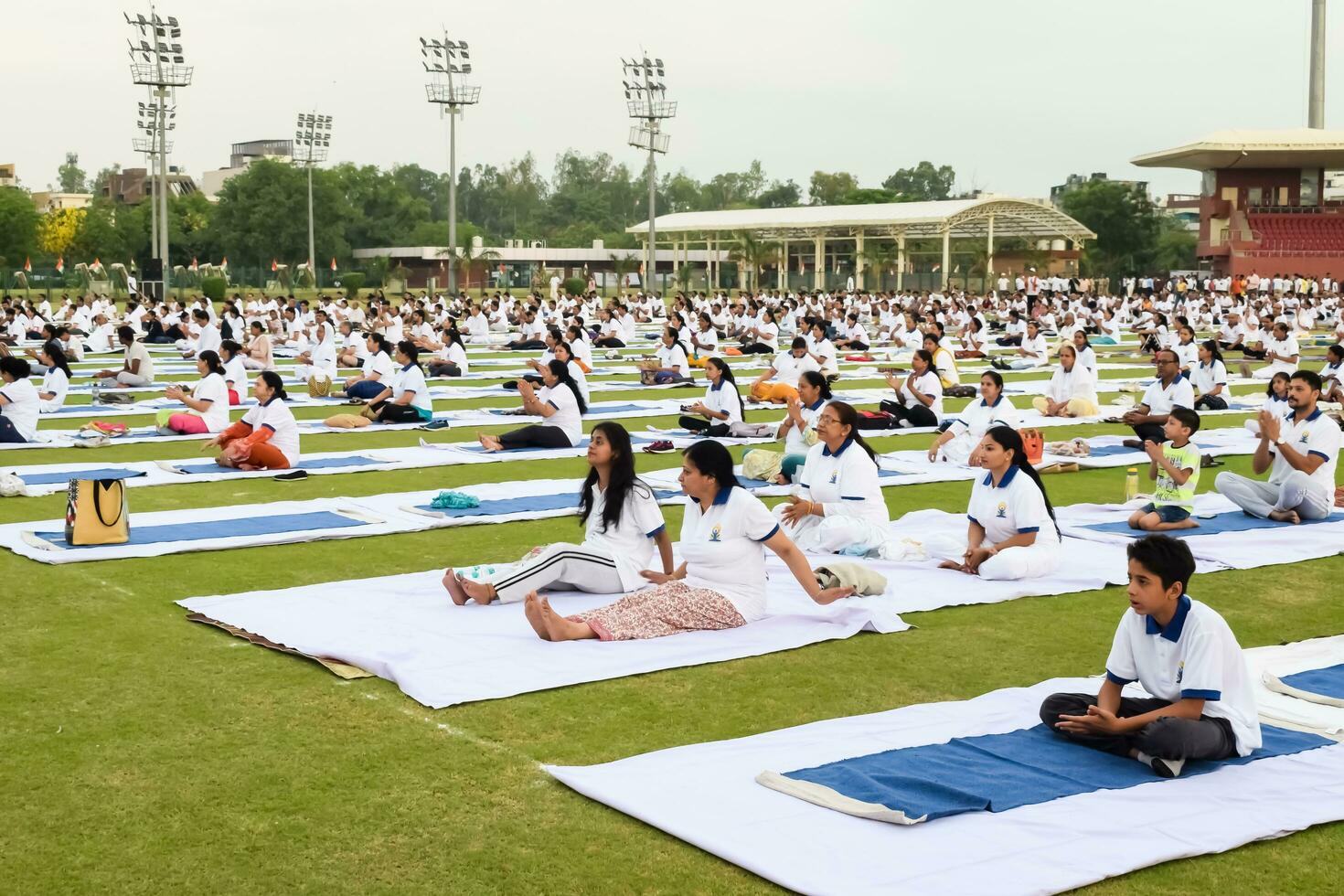 New Delhi, India, June 21, 2023 - Group Yoga exercise session for people at Yamuna Sports Complex in Delhi on International Yoga Day, Big group of adults attending yoga class in cricket stadium photo