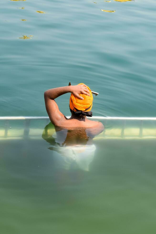 Amritsar, India - February 26 2023 - Unidentified devotees taking holy dip in sarovar at Golden Temple - Harmandir Sahib in Amritsar, Punjab, India, Famous indian sikh landmark, Golden Temple photo
