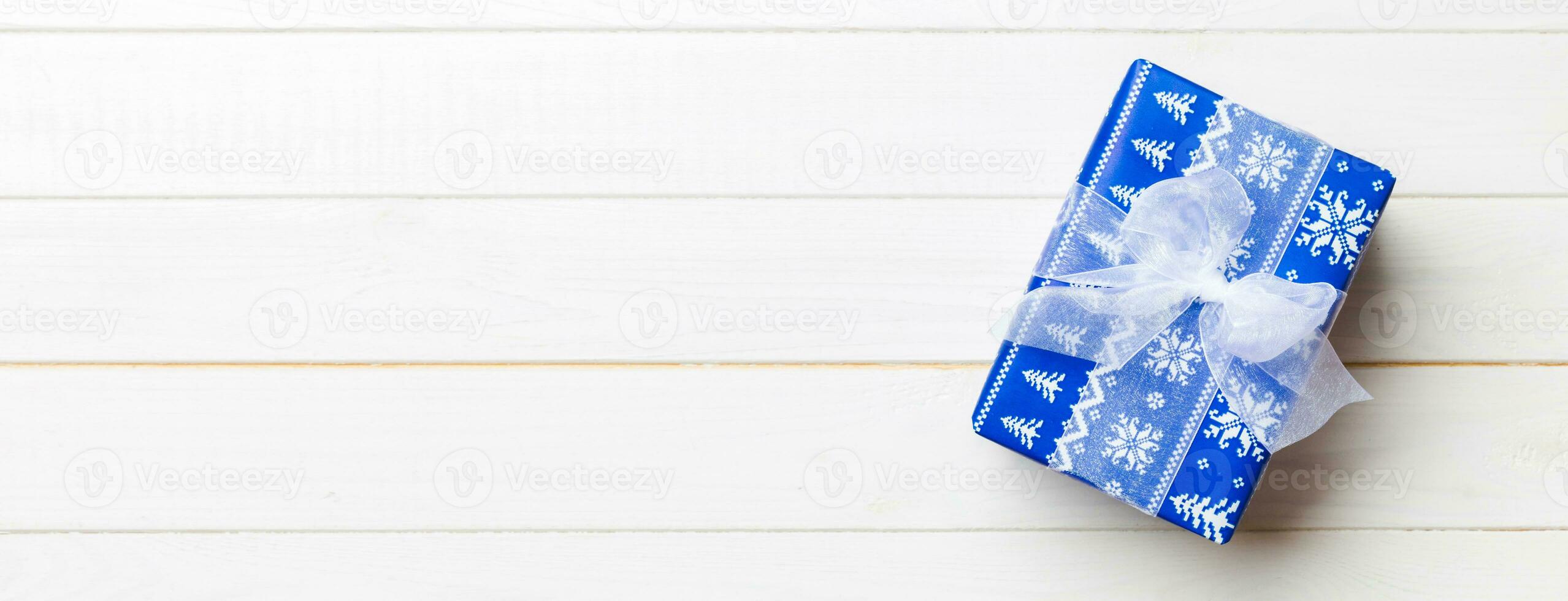 Beautiful gift box with a colored bow on the white wooden table. Top view with copy space for you design. Christmas concept photo