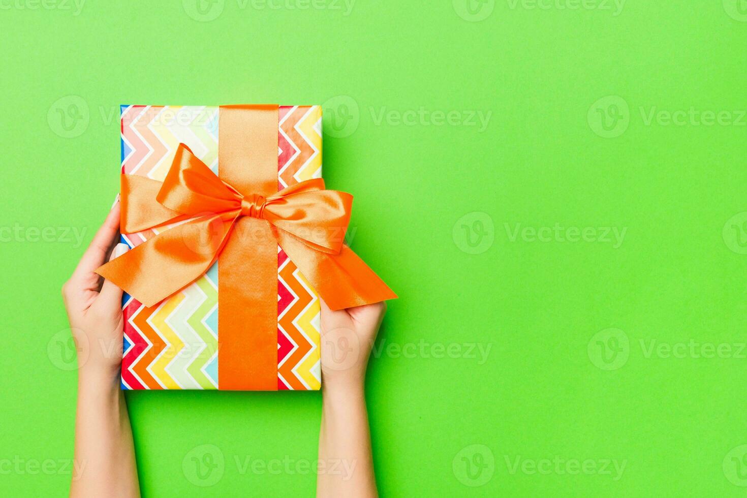 Top view of female hands holding christmas or other holiday handmade present box package in the palms, flat lay table background with copy space photo