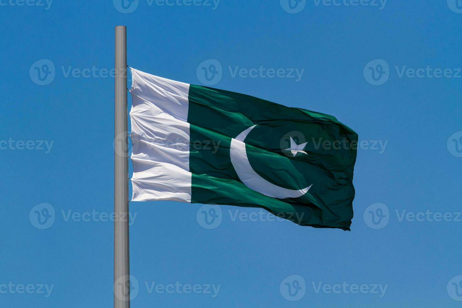 Flag of Pakistan waving in the wind on a pole against blue sky photo