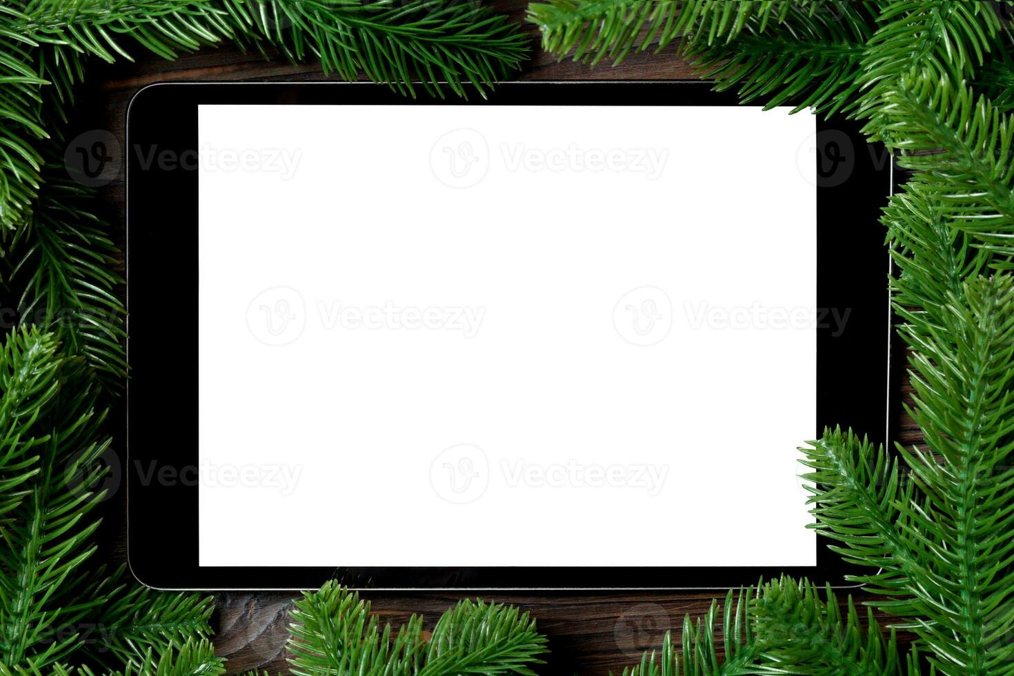 Top view of tablet decorated with a frame made of fir tree on wooden background. New Year time concept photo