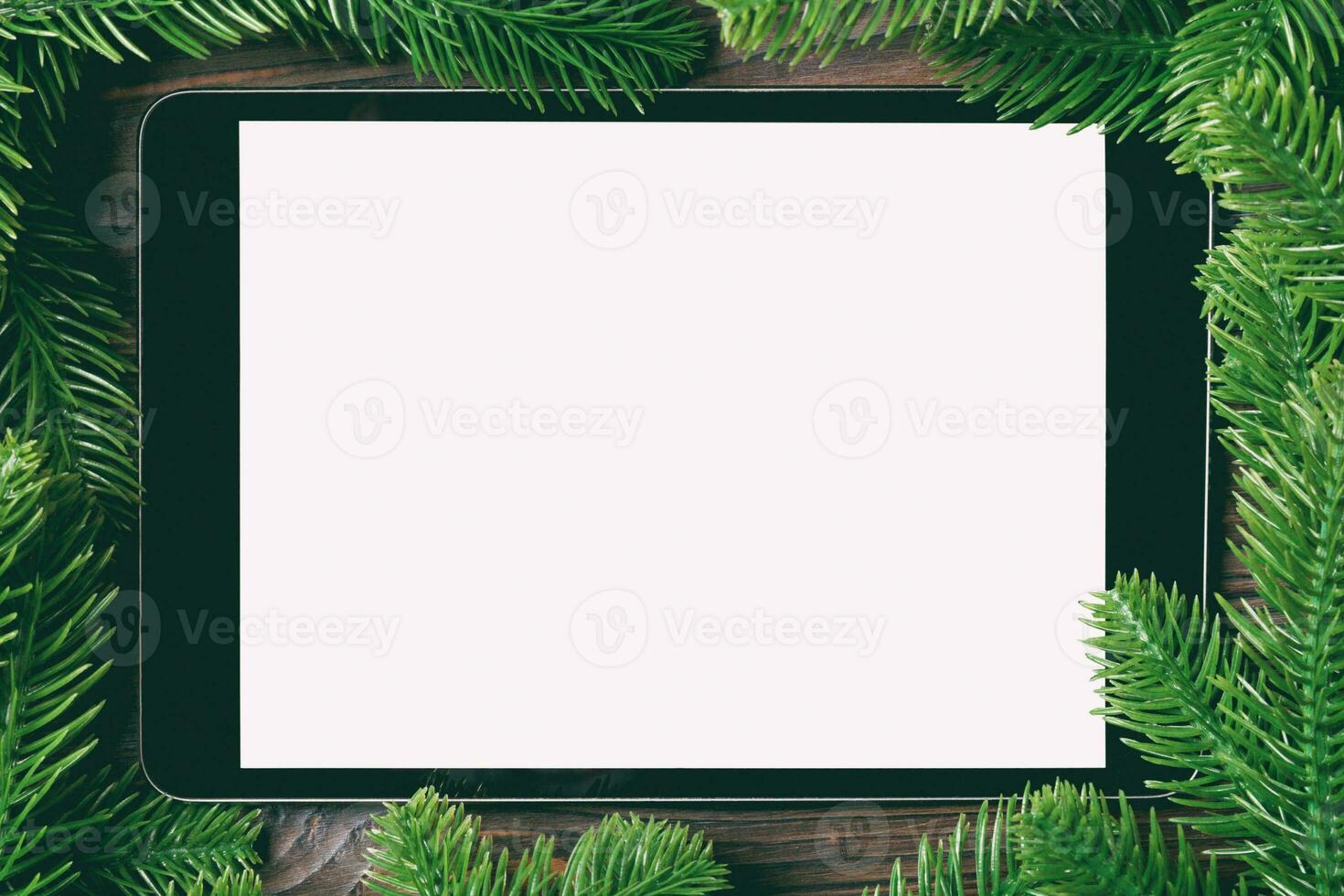 Top view of tablet decorated with a frame made of fir tree on wooden background. New Year time concept photo