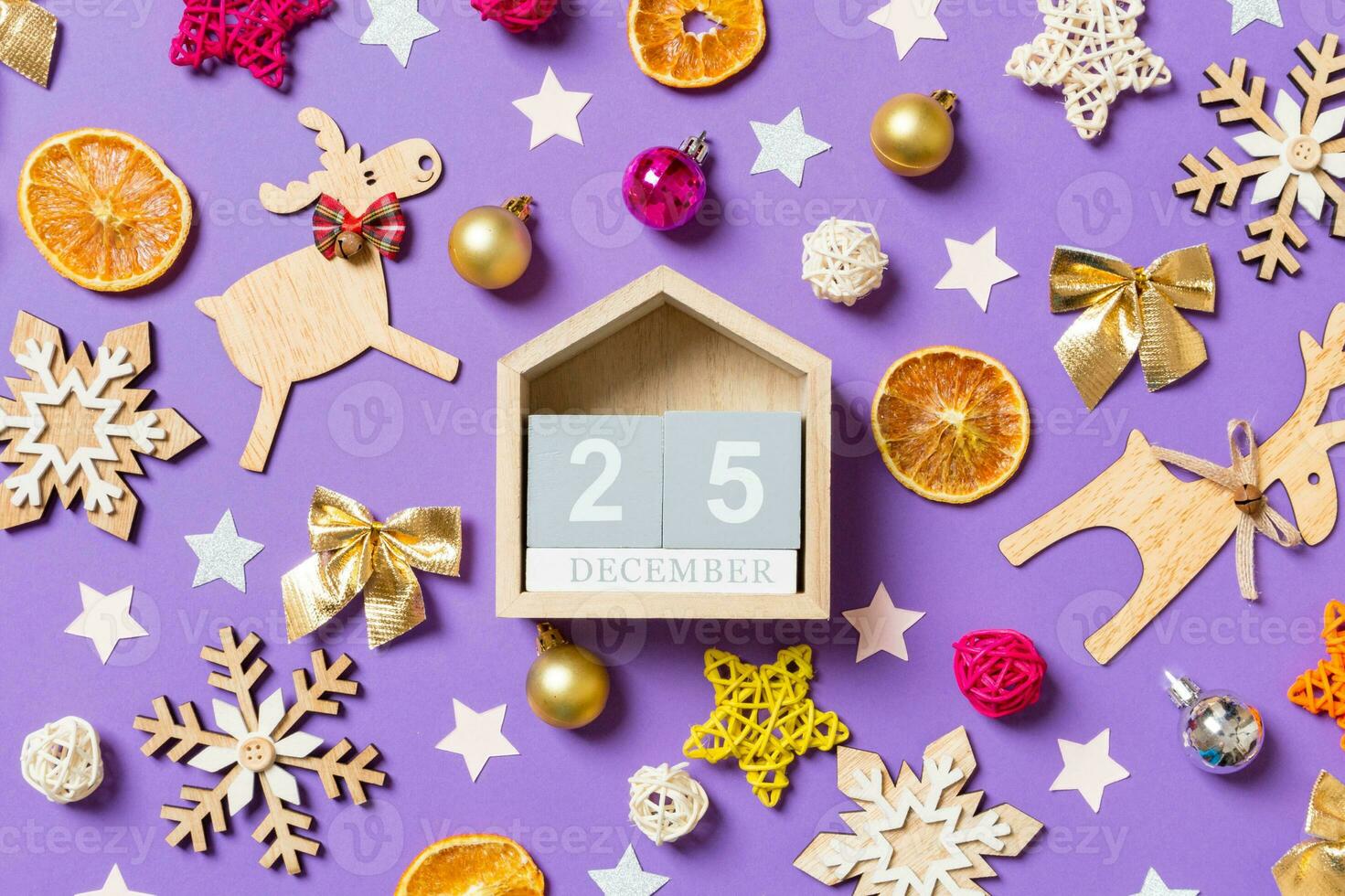 Top view of wooden calendar surrounded with New Year toys and decorations on purple background. The twenty fifth of December. Christmas time concept photo