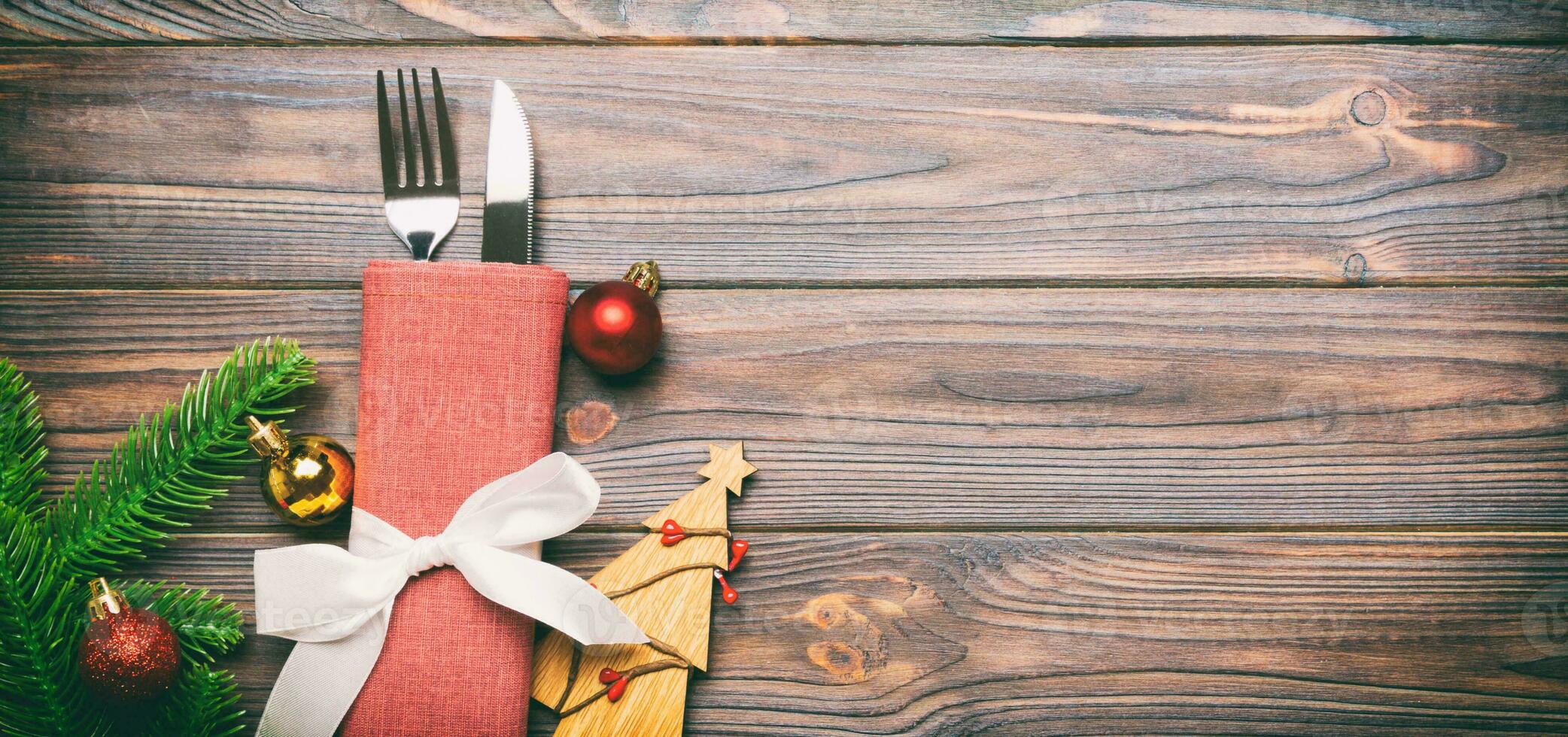 Top view Banner of fork and knife on napkin with christmas decorations and new year tree on wooden background. Holiday and festive concept with copy space photo