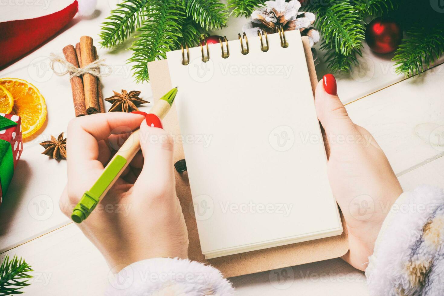 Top view of female hand writing in a notebook on wooden Christmas background. Fir tree and festive decorations. Wish list. New Year concept photo