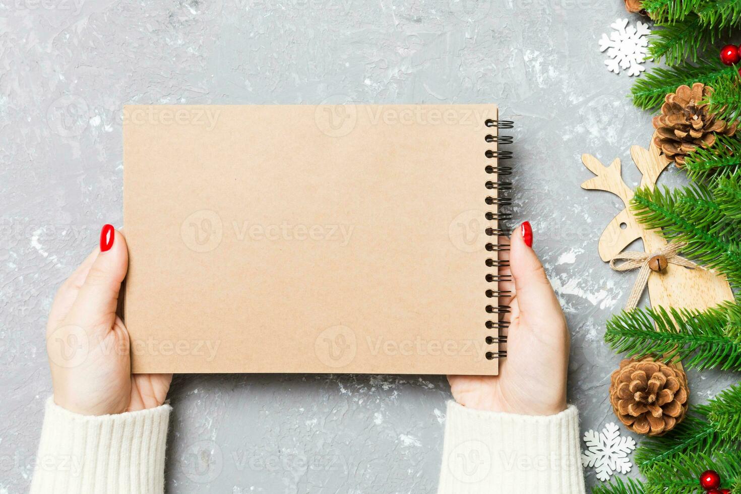 Top view of female hand holding a notebook on cement Christmas background. fir tree and festive decorations. Wish list. New Year concept photo