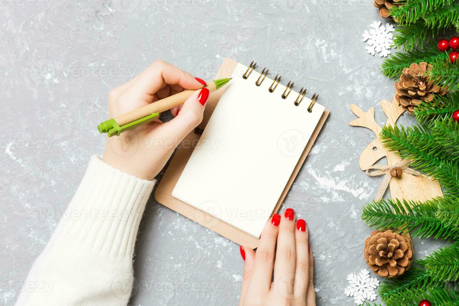Top view of female hand writing in a notebook on cement Christmas background. fir tree and festive decorations. Wish list. New Year concept photo