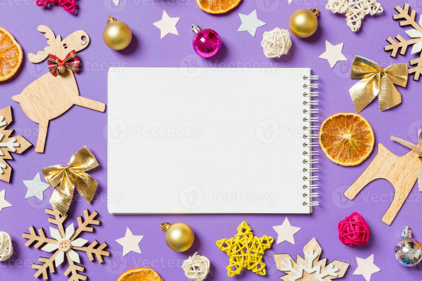 Top view of notebook surrounded with New Year toys and decorations on purple background. Christmas time concept photo